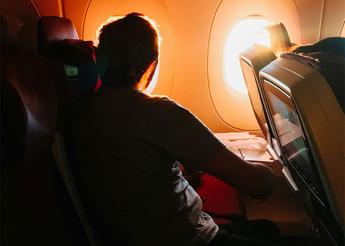 Person sitting on an airplane, looking out the window during sunset, contemplating the need to leave quickly.
