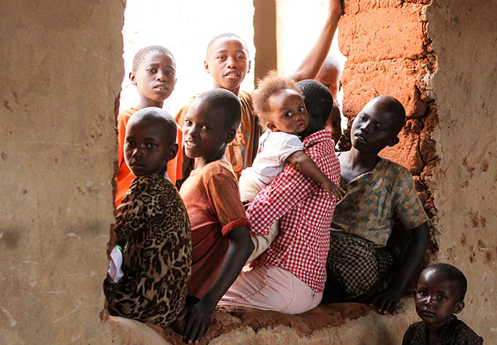 Group of children in a rustic setting, sitting together and observing something outside.