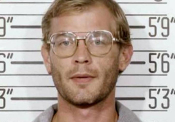 Mugshot of a man with glasses standing against a height chart, related to disturbing facts and uncomfortable truths.