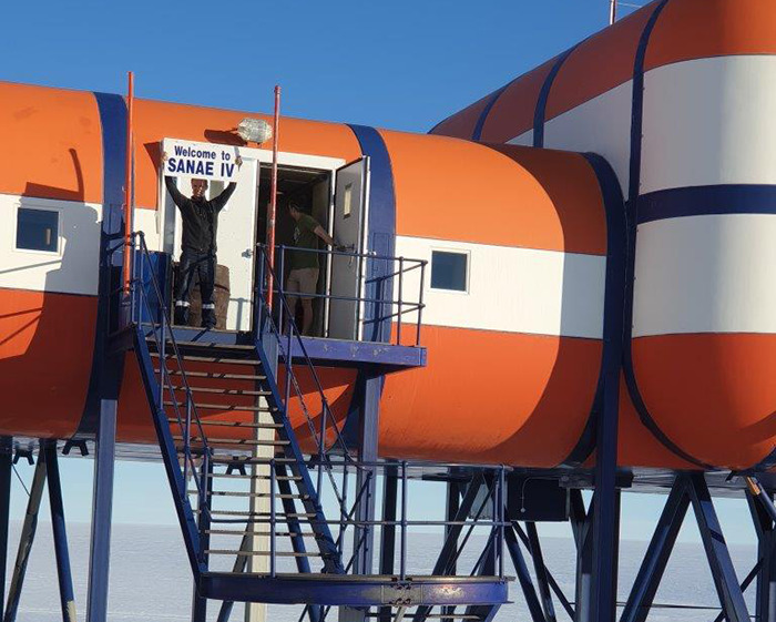 Entrance to SANAE IV base in Antarctica with stairs and scientists at the doorway.