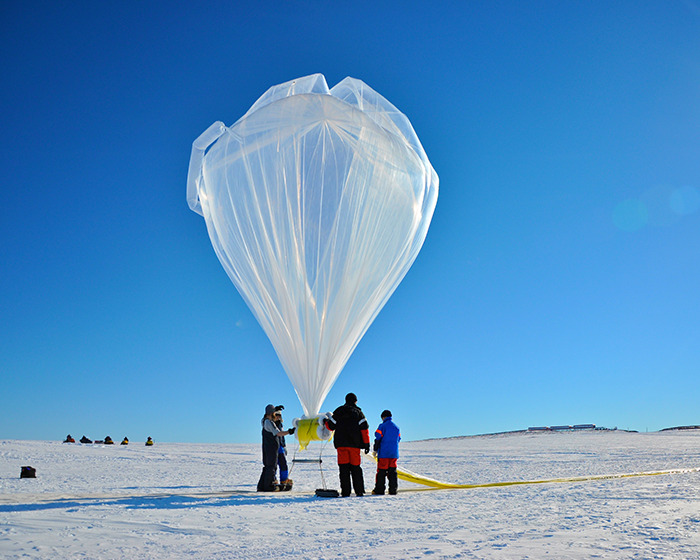 Scientists in Antarctica prepare a large weather balloon under a clear blue sky.