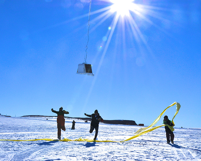Scientists in Antarctica working under the sun with equipment suspended in the sky above them.