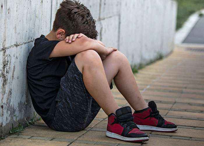 A young boy in red sneakers sits sadly against a wall, suggesting family discipline issues.