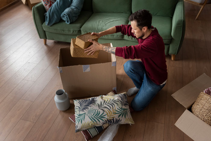 Man packing boxes in a living room, possibly signaling relationship tension or a move related to divorce issues.