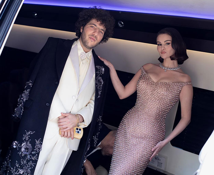 Benny in a white suit and floral coat, standing with a woman in a sparkling gown, showcasing elegance and style.