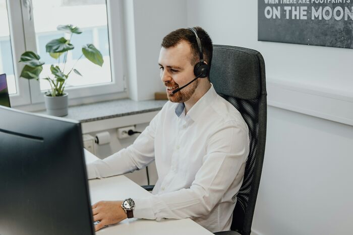 Man in white shirt with headset working at a desk, addressing job misconceptions on a video call.