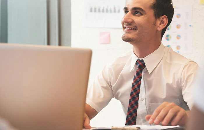 Smiling man in an office setting, wearing a white shirt and tie, symbolizing stories about difficult bosses.