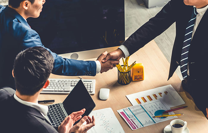 Business meeting with a focus on bosses; two men shaking hands over a conference table with documents and a laptop.