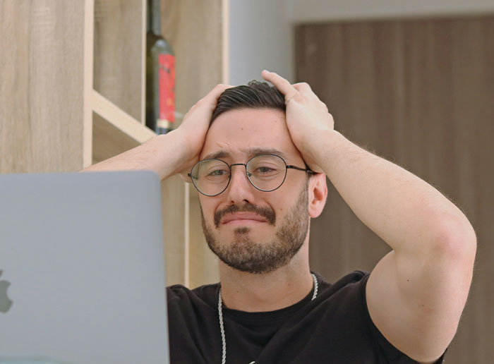 Man in glasses looking stressed at laptop, hands on head; represents "Bosses From Hell" experiences.