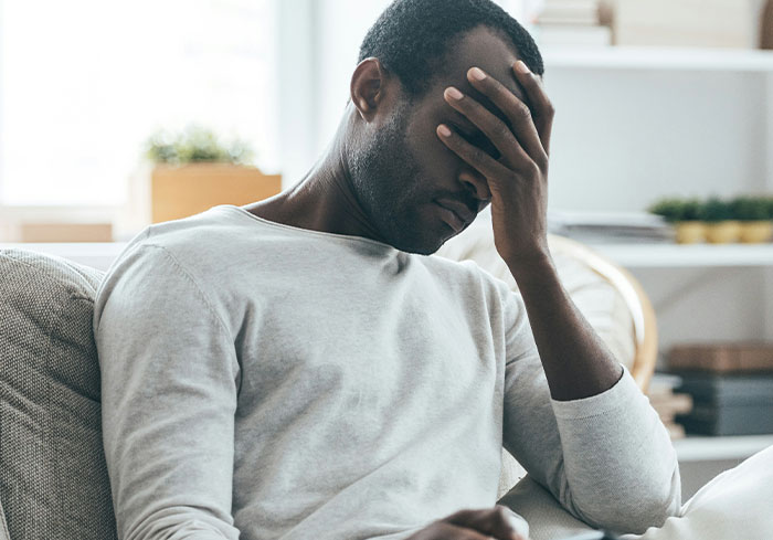 Man in gray shirt looking stressed, hand on face, in living room, symbolizing stories of bosses from hell.