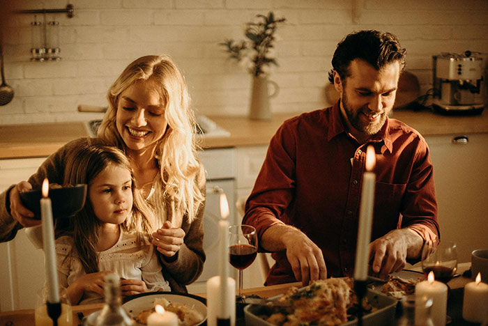 Family dinner in cozy kitchen setting, parents with child, warm lighting, laughter and togetherness.