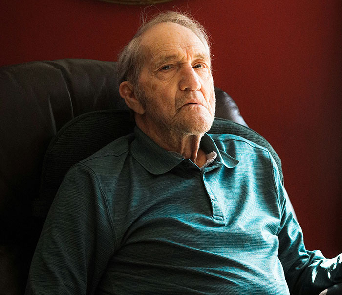 Un hombre mayor con expresión seria, sentado en un sillón, iluminado por la luz, sugiriendo experiencias de trauma.