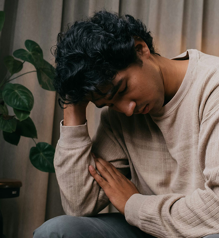 Persona pensativa con gesto de tristeza, sentada en una habitación con plantas. Indicativo de traumas pasados.