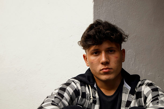 Young man with a thoughtful expression, wearing a checkered shirt, possibly reflecting signs of trauma.