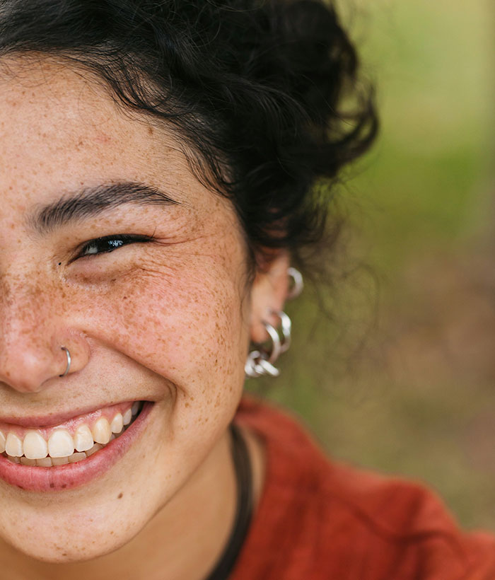 Smiling person with freckles and curly hair, showcasing signs of resilience and trauma experience.