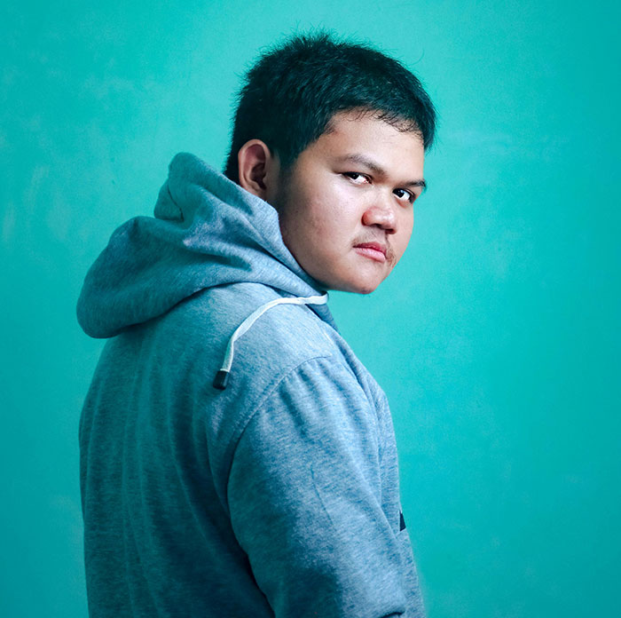 Persona en suéter gris mirando hacia atrás, reflejando señales de traumas pasados en pared azul de fondo.