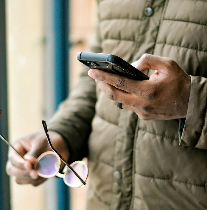 Man in green jacket holding phone and sunglasses, possibly indicating signs of trauma through body language.