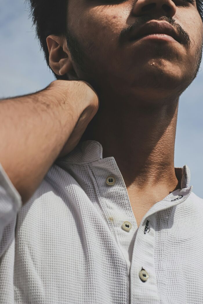 Man in white shirt touching neck, sunlight highlighting facial features.