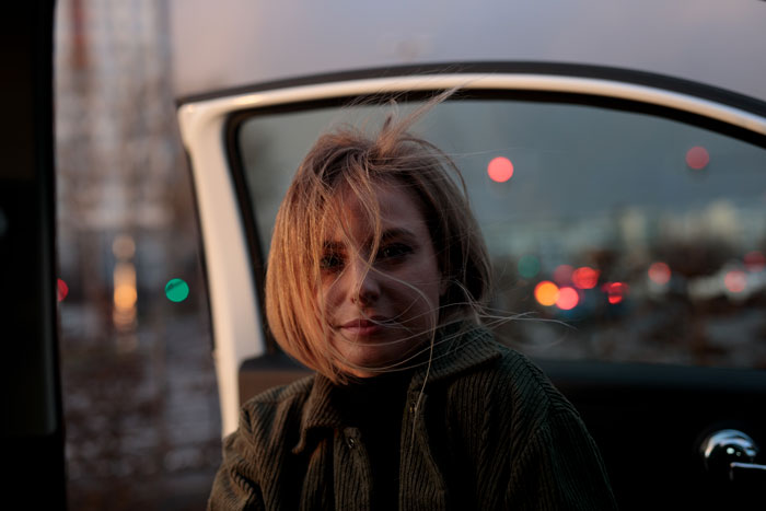 Woman in car at night, facing consequences after driving off road, sibling unsympathetic.