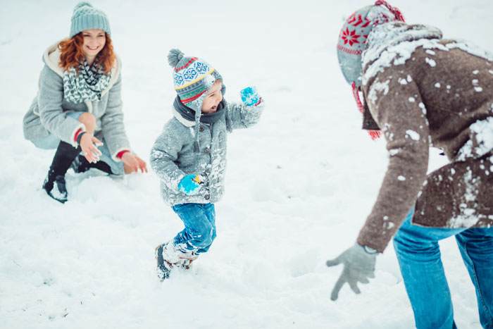 Child playing in snow with adults, bundled up in winter clothing, having fun on a snowy day.