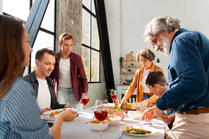 Family gathering at table with food and drinks, lively discussion unfolding among the group.