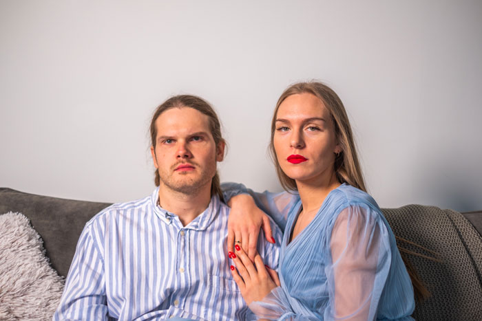 A man and woman sitting on a couch; the man looks flabbergasted.