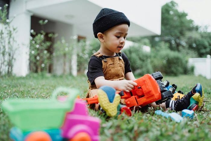 Child playing with toys outside on grass, wearing overalls and a beanie. Child playing with toys outside on grass, wearing overalls and a beanie.