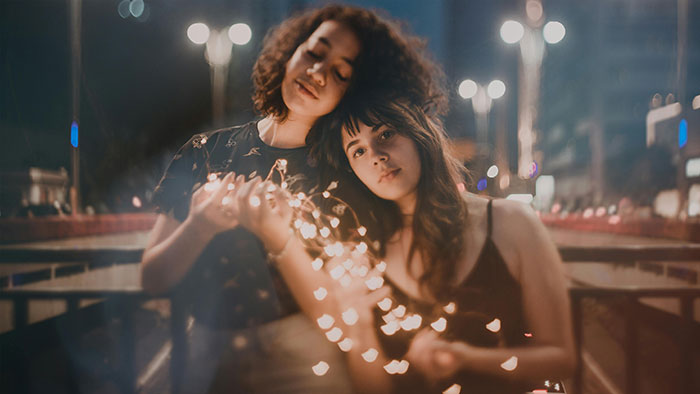 Two women with fairy lights at night, looking thoughtful, related to bridesmaid fee discussion.