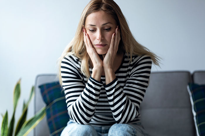 Woman in striped shirt sitting on a couch, looking contemplative about babysitting boundaries.