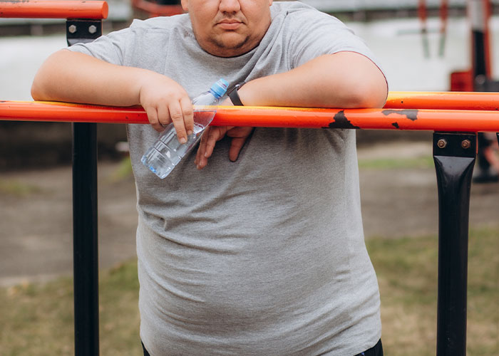 Man in a grey shirt leaning on an orange bar, holding a water bottle, symbolizing unknown small town incidents.