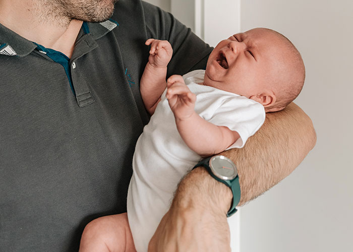 A man in a gray shirt cradles a crying baby, symbolizing small town incidents.