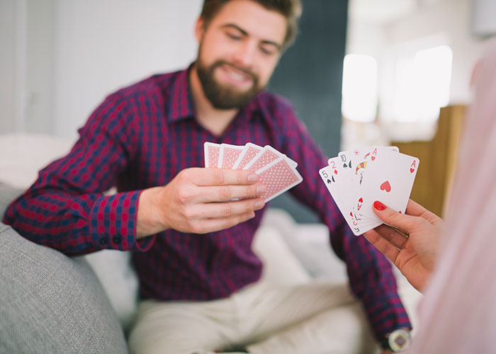 Man in plaid shirt playing cards, smiling in a close-knit setting, reflecting on small town incidents.