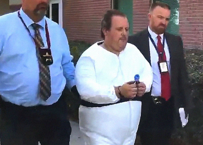 A man in a white outfit is escorted by two men, related to a small town incident.