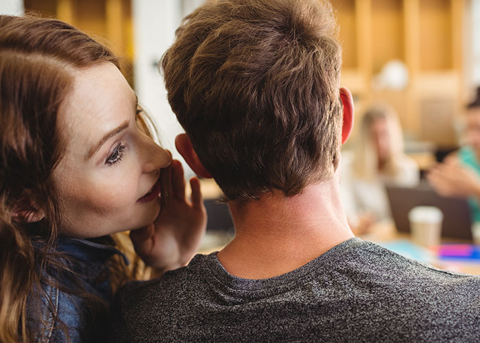 A woman leans in to whisper to a man, representing a small town secret or incident.