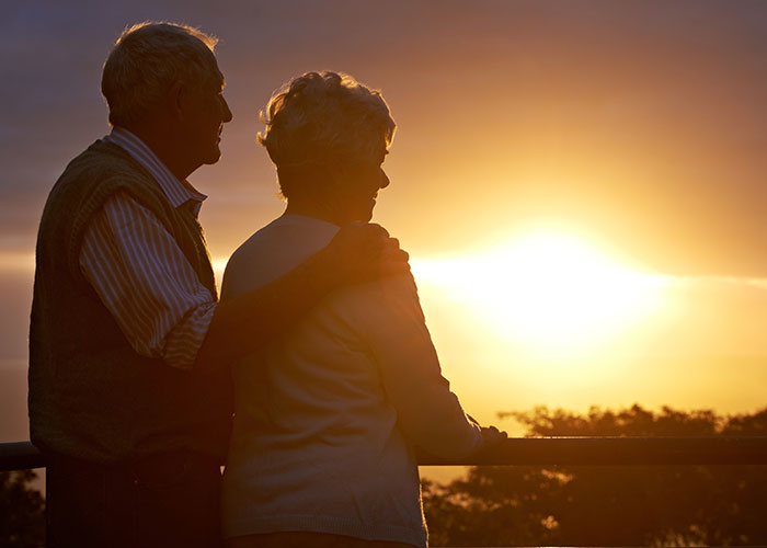 Elderly couple embracing, watching sunset, symbolizing small town secrets and untold incidents.