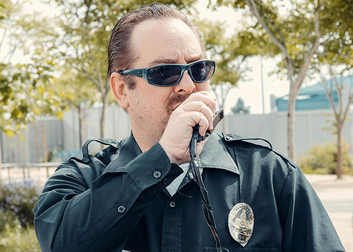 Police officer in uniform and sunglasses uses a radio, addressing a small town incident.