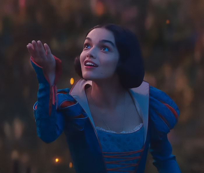 Snow White character in a blue dress reaches outwards against a blurred forest backdrop in Disney's movie scene. Snow White character in a blue dress reaches outwards against a blurred forest backdrop in Disney's movie scene.