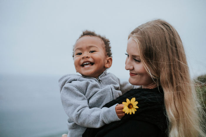 A smiling woman holding a joyful child near the ocean, highlighting themes of family dynamics and relationships. A smiling woman holding a joyful child near the ocean, highlighting themes of family dynamics and relationships.