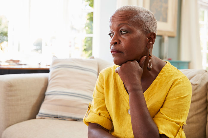 Elderly woman sitting thoughtfully on a couch, dressed in a yellow top in a cozy living room. Elderly woman sitting thoughtfully on a couch, dressed in a yellow top in a cozy living room.
