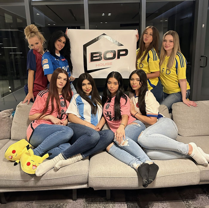 Group of seven young women posing with a "BOP House" sign, showcasing online influence mastery.