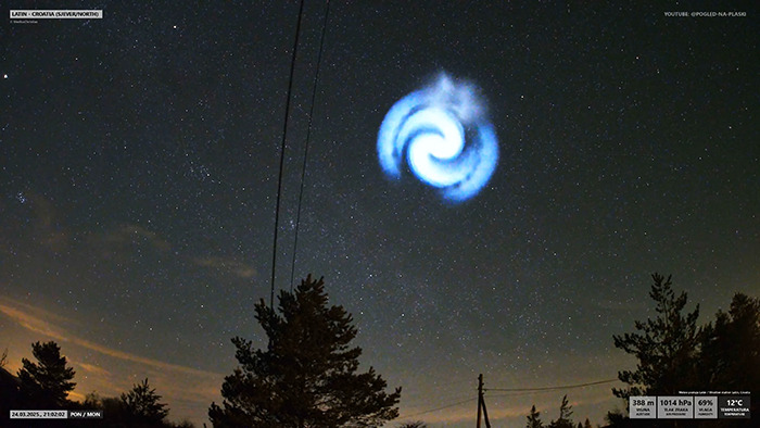 Mysterious spiral in UK sky, glowing bright against a starry night backdrop and trees.