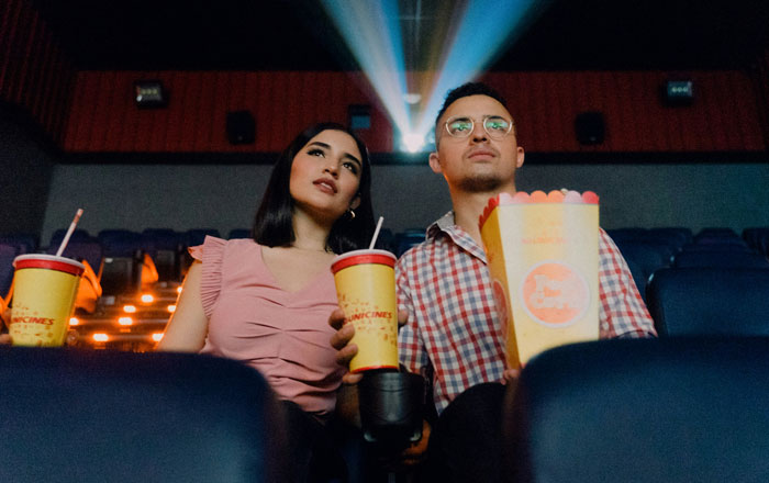 Moviegoers with popcorn and drinks, looking at the screen in a dimly lit theater.