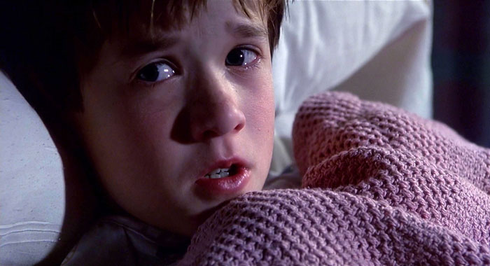 A child looks worried under a pink blanket, eyes wide open in the dim light.