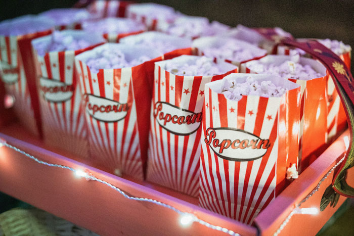 Movie popcorn in red and white striped bags on a pink tray, representing a theater setting.