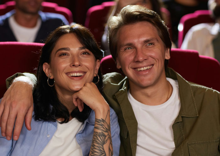 Couple enjoying a movie in a theater, surrounded by red seats, highlighting the main character experience.