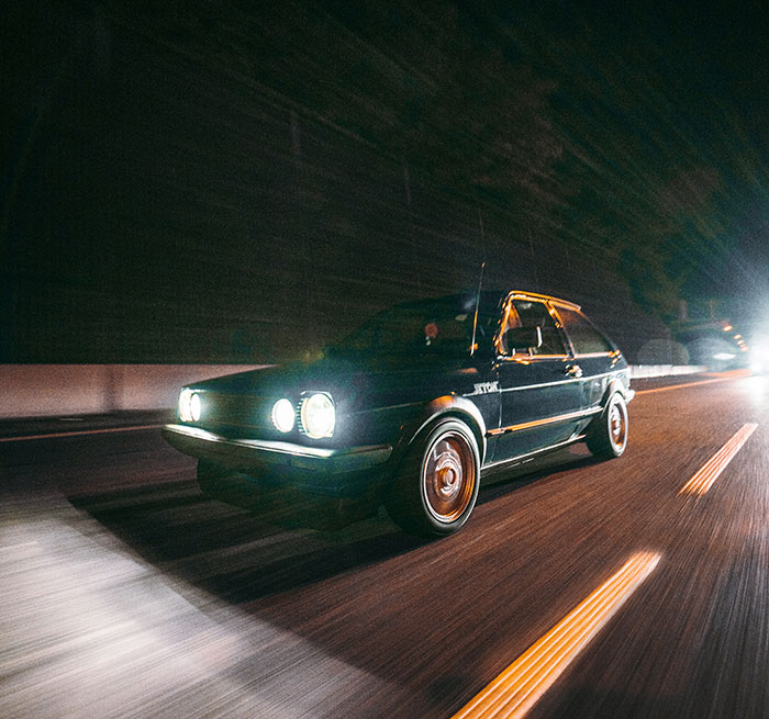 Coche clásico circulando de noche en carretera, representando personas que aún siguen vivas por decisiones espontáneas.