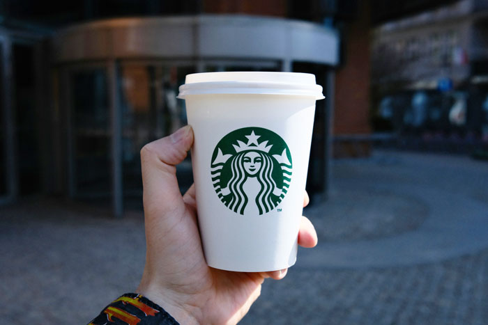 Hand holding a Starbucks cup outdoors, related to severe burn case and $50M verdict.