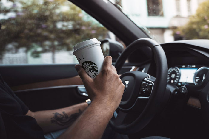 Person holding a Starbucks cup while driving, illustrating customer experience and coffee culture.