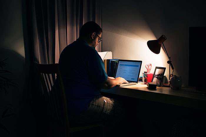 Man working on a laptop at night in a dimly lit room, experiencing a change in lifestyle. Man working on a laptop at night in a dimly lit room, experiencing a change in lifestyle.