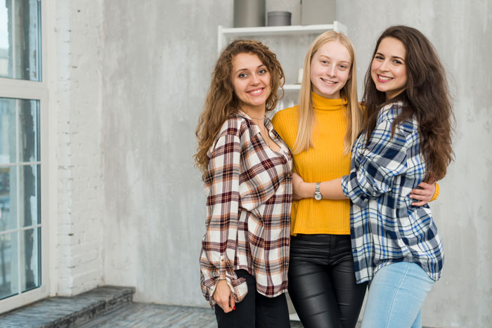 Three women smiling and embracing, wearing casual clothes, in a cozy, bright room, conveying family dynamics and relationships.